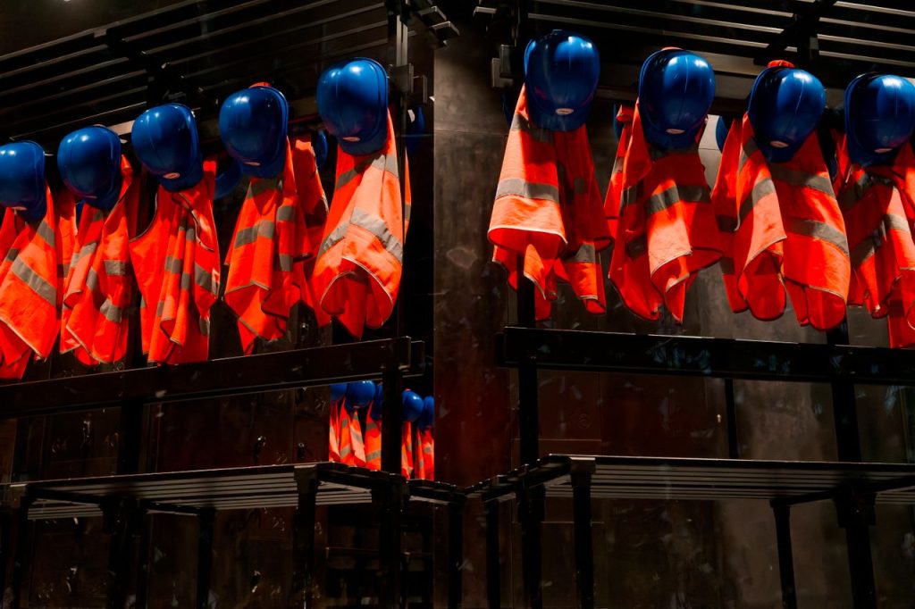 Row of orange safety vests and blue helmets hanging in industrial setting